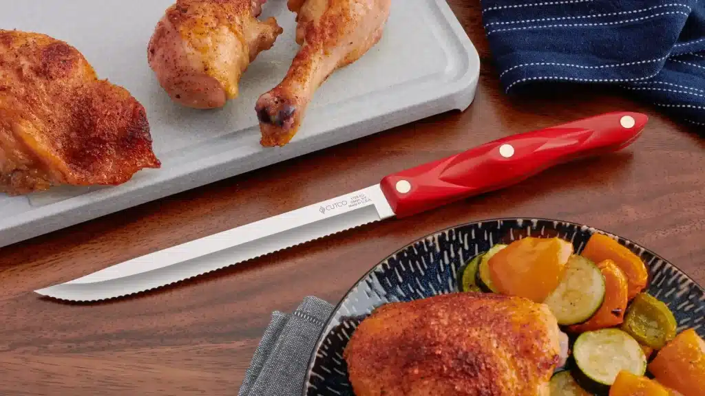 Serrated carving knife with red handle beside roasted chicken and vegetables