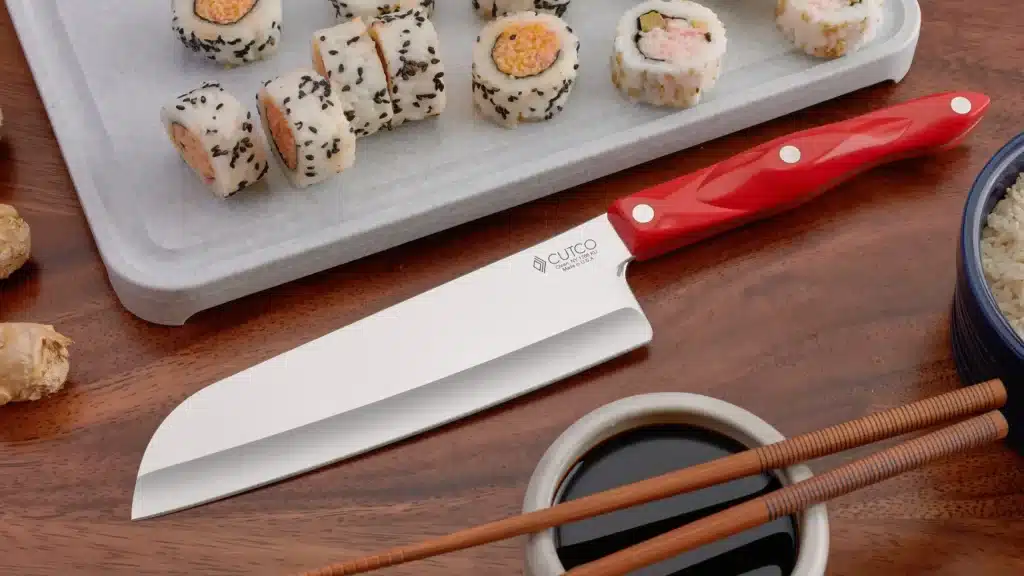 Red-handled santoku knife displayed beside sushi rolls, soy sauce, and chopsticks