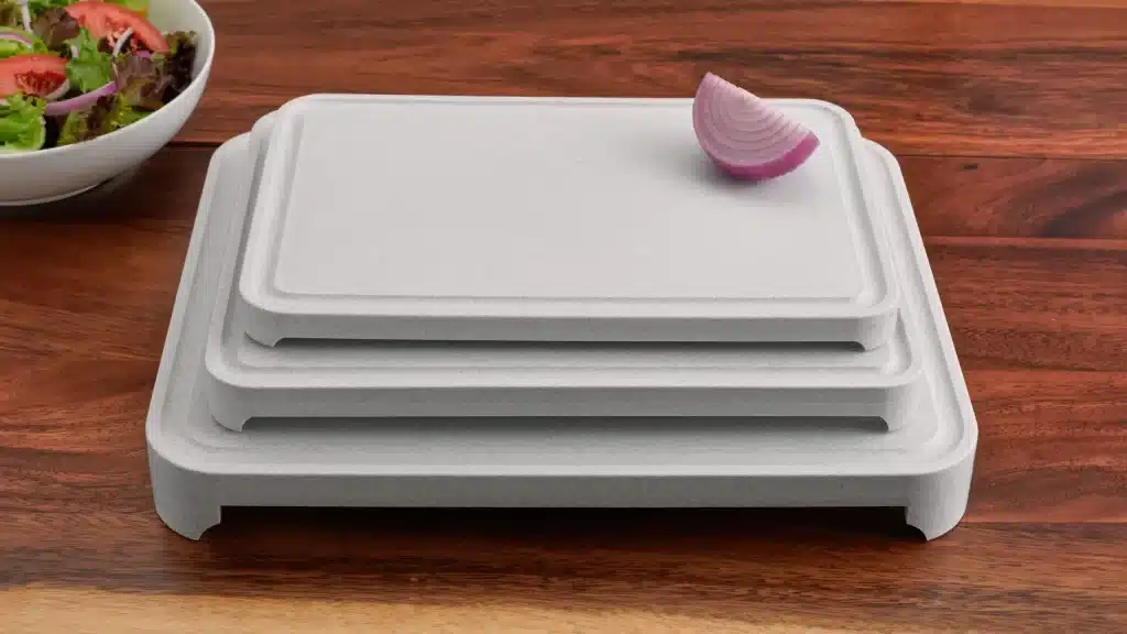 Stacked gray cutting boards on a wooden countertop with sliced red onion