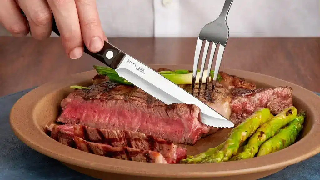 cutco steak knife slicing medium rare steak with asparagus on dinner plate