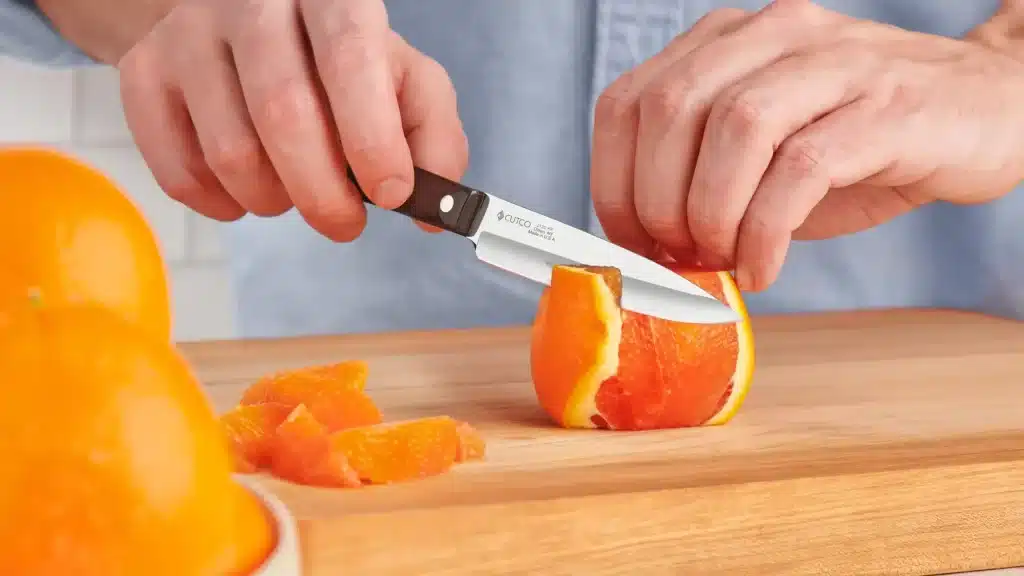 cutco paring knife peeling an orange on a wooden cutting board