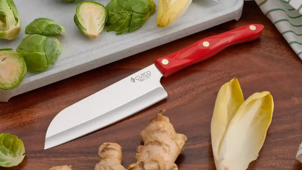 cutco santoku knife with red handle on wooden surface with brussels sprouts and ginger