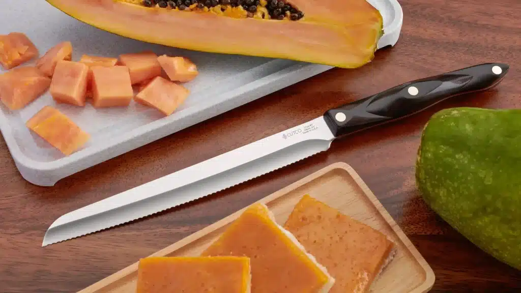 cutco serrated knife on wooden surface with sliced papaya and mango